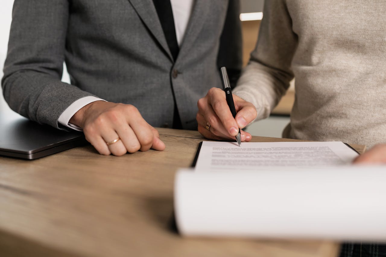 Home Close-up of businessmen signing documents at a wooden table in an office.