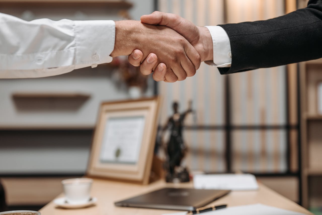 Offerings Close-up of a handshake between two professionals in a modern office setting, emphasizing partnership and agreement.